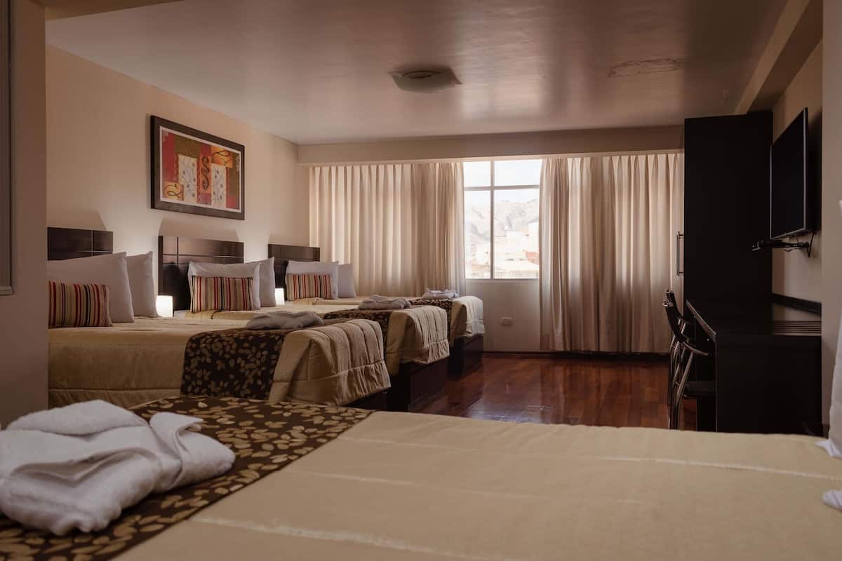 Une chambre d’hôtel avec deux lits, un téléviseur à écran plat, un bureau et une fenêtre avec des rideaux.