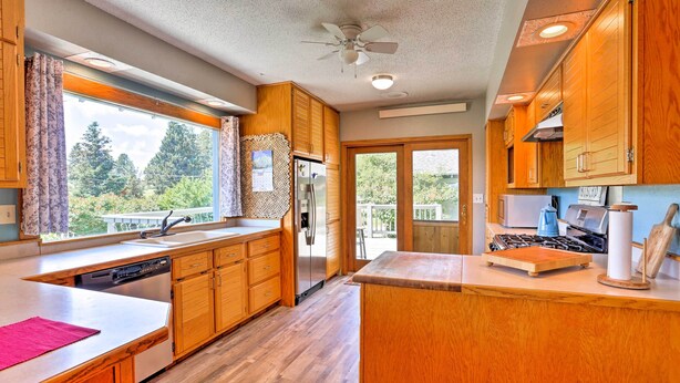 A kitchen with wooden cabinets, a dishwasher, a refrigerator, a stove, and a window with a view of trees.