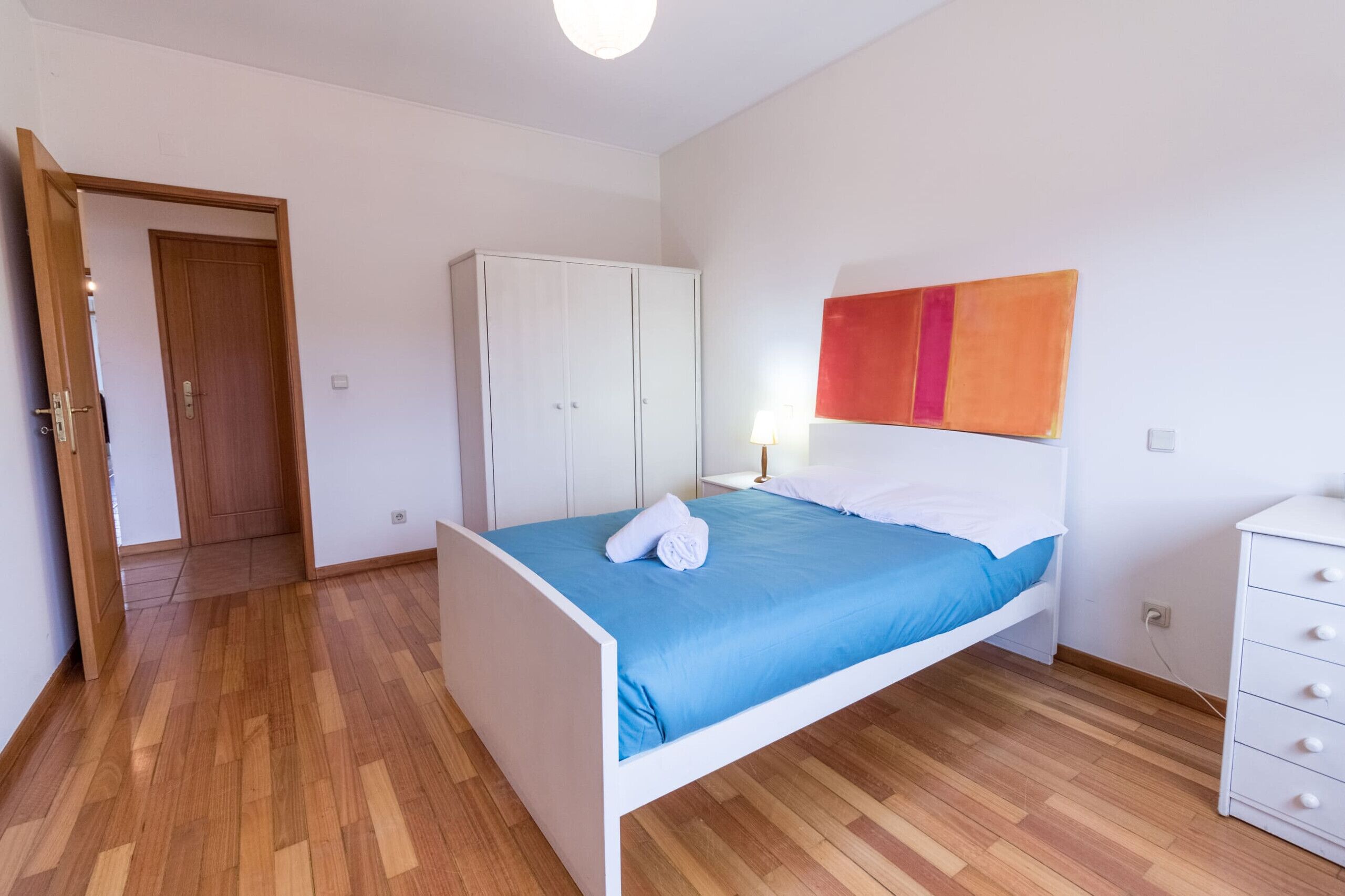 Un dormitorio con cama, armario, mesita de noche y cómoda.