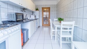 Une cuisine moderne avec des meubles blancs, un four encastré, un four à micro-ondes et une cuisinière à gaz. On y trouve une table à manger avec des chaises et une plante en pot.