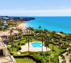 A resort with a pool, palm trees, and a view of the ocean.