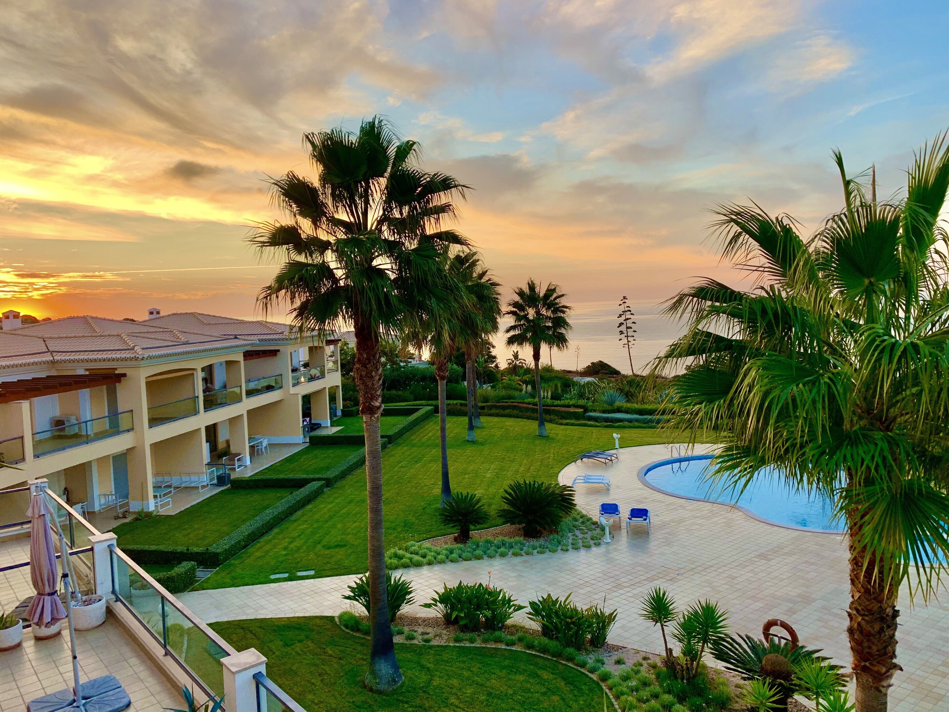Un hotel con piscina, palmeras y vistas al atardecer.