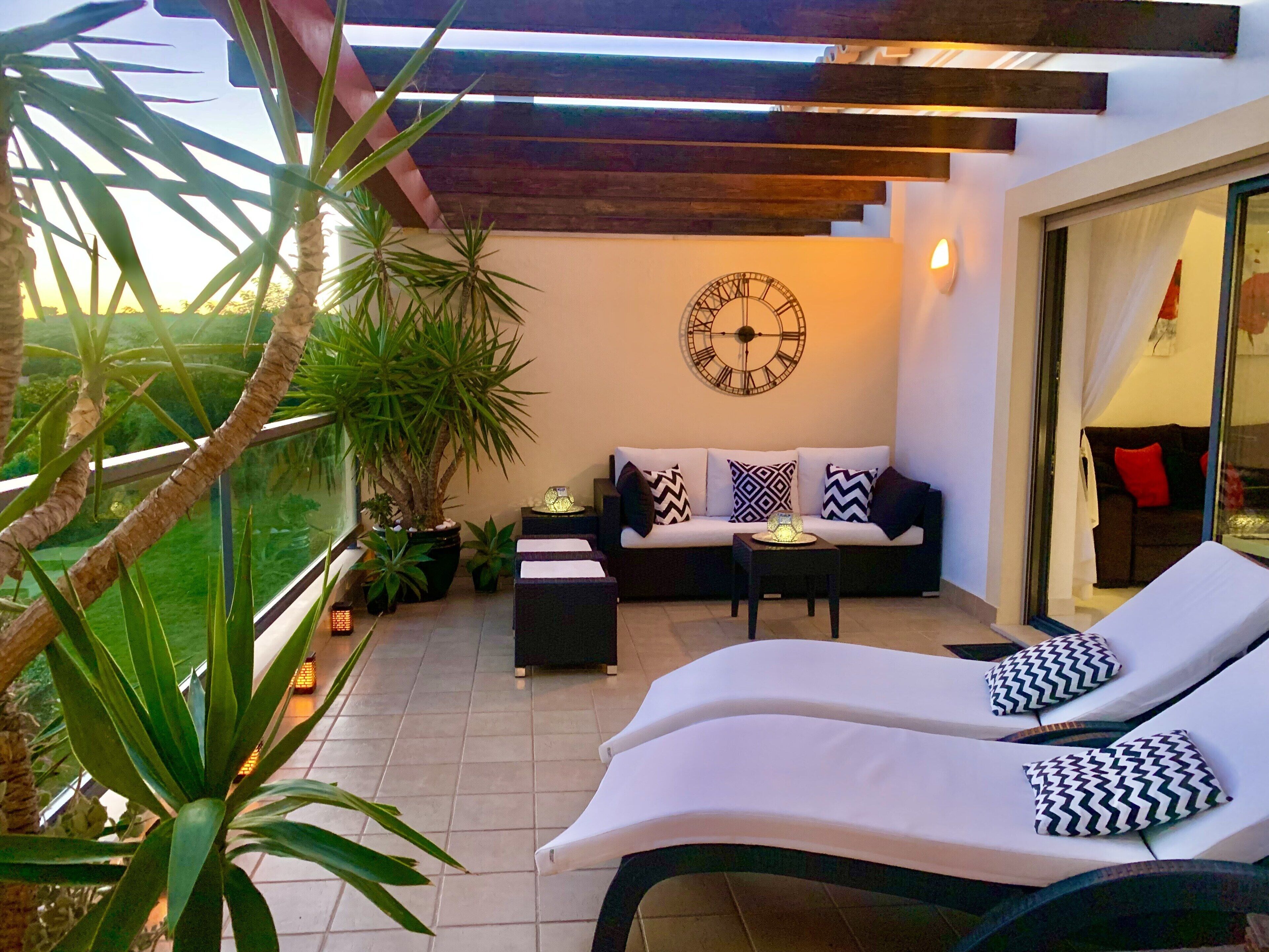 A modern outdoor lounge area with a sofa, two lounge chairs, a table, and potted plants.