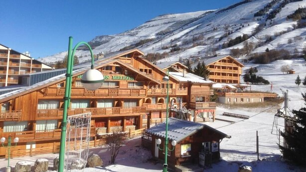 Un bâtiment de style chalet en bois, doté de balcons, avec une piste de ski en arrière-plan.