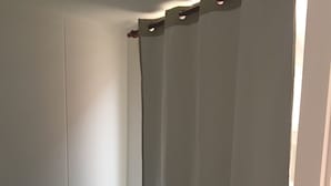 Une petite chambre avec un lit simple, une couvre-lit turquoise, un rideau blanc et un mur blanc.