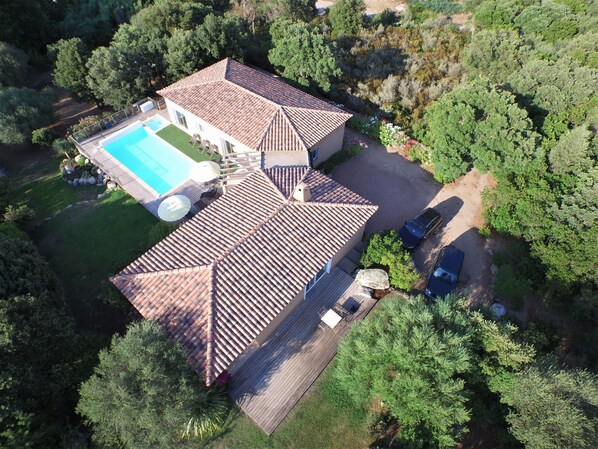 An aerial view of a house with a swimming pool, a covered patio, and a car parked in the driveway.