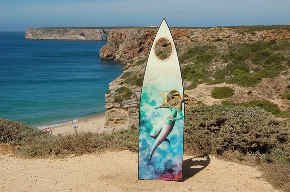 A surfboard sculpture with a dolphin design on a beach with a cliff and ocean in the background.