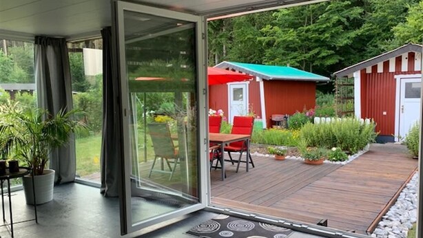 Una casa moderna con una puerta de cristal que da a una terraza de madera.