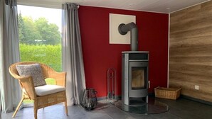 Una habitación con pared roja, una chimenea moderna, un sillón de mimbre y vistas al exterior con vegetación.