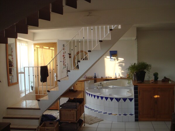 Amplia sala de estar con una escalera que lleva a un segundo piso, una bañera grande y un armario de madera.