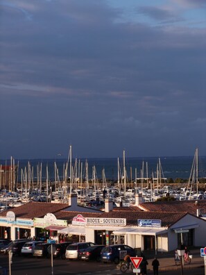 A marina with numerous boats docked, a souvenir shop, and a few cars parked in the foreground. - APARTEMENT ILE DE NOIRMOUTIER 'Port de l'Herbaudière' 2 pers (Noirmoutier-En-L'île)