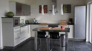 Eine moderne Küche mit weißen Schränken, einer zentralen Kochinsel mit Hockern, einer Mikrowelle, einer Kaffeemaschine und einem Kühlschrank.