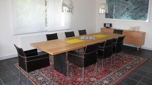Ein moderner Essraum mit einem Holztisch, schwarzen Stühlen, einem roten Teppich mit Muster und einem großen abstrakten Gemälde an der Wand.