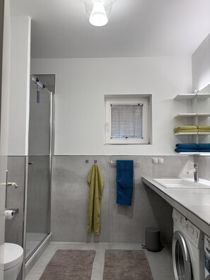 Ein modernes Badezimmer mit Duschkabine aus Glas, Toilette, Waschbecken mit Spiegel, Fenster und Waschmaschine.