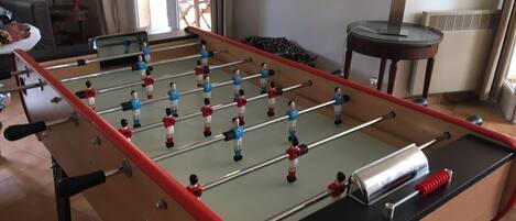 Una mesa de fútbol de mesa en una habitación con ventana, un radiador y una pequeña mesa con una planta.