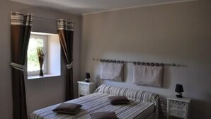 Quarto com cama, cortinas, janela, mesa de cabeceira e porta-toalhas fixado na parede.
