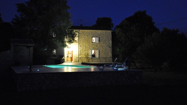 Um edifício de pedra com piscina e espreguiçadeiras à noite.