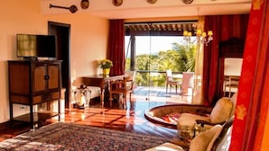 A spacious living room with a large rug, a sofa, and a television on a wooden cabinet. There is a balcony with a view of greenery. - Villa Felicche Búzios (Búzios)