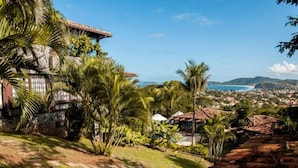 A coastal property with a stone house, lush greenery, and a view of the sea and distant hills. - Villa Felicche Búzios (Búzios)