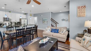 A modern living room with a dining area, kitchen, and a staircase leading to another level. - Blue Mountain Beach, Sleeps 12, Steps from Pool + Free Attraction Tickets! (Santa Rosa Beach)