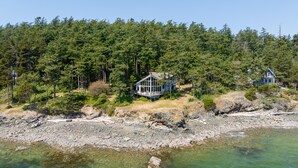 Propiedad costera con dos casas rodeadas de un bosque denso, una costa rocosa y aguas cristalinas.
