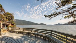 A wooden deck with benches overlooking a calm lake, surrounded by trees and hills. - Orcas Island, Juniper House #212 (Eastsound)