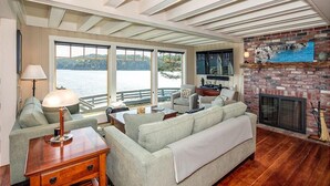 A living room with a large window overlooking a body of water, a fireplace, and a wooden floor. - Orcas Island, Juniper House #212 (Eastsound)