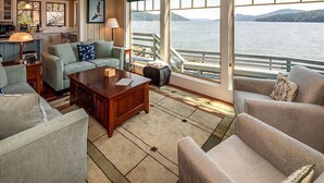 A spacious living area with a large window overlooking a body of water, a cozy seating arrangement, and a visible kitchen area. - Orcas Island, Juniper House #212 (Eastsound)