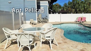 Ein Poolbereich mit Korbmöbeln und Blick auf ein Haus mit der Aufschrift 'Apt. Pelican'.