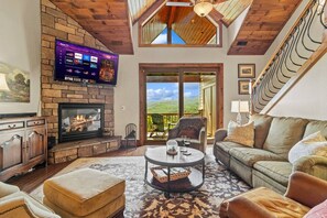 A cozy living room with a fireplace, a television mounted on the wall, and a balcony with a view of the outdoors.