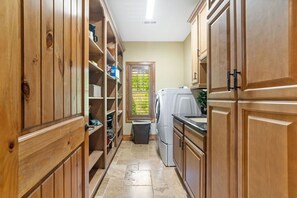 A narrow kitchen with wooden cabinets, a washing machine, and a window with a view of greenery.