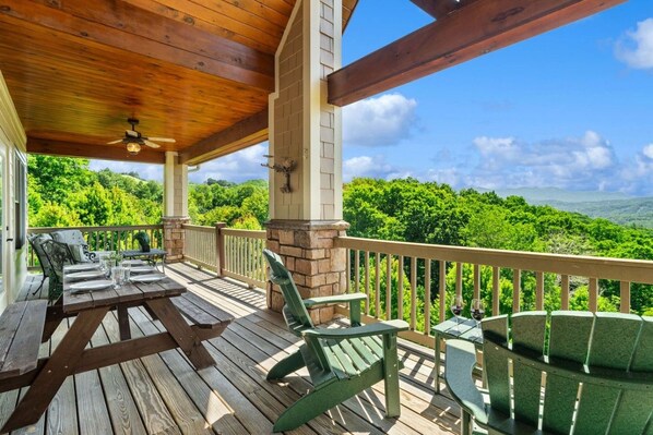 A covered outdoor area with wooden flooring, green chairs, and a table set for dining.