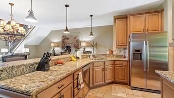 A kitchen with granite countertops, wooden cabinets, a stainless steel refrigerator, and pendant lighting.