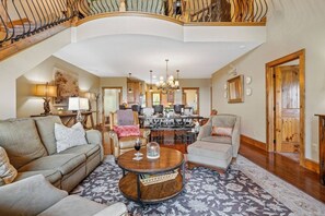 A spacious living room with a high ceiling, a dining area, and a staircase leading to an upper level.