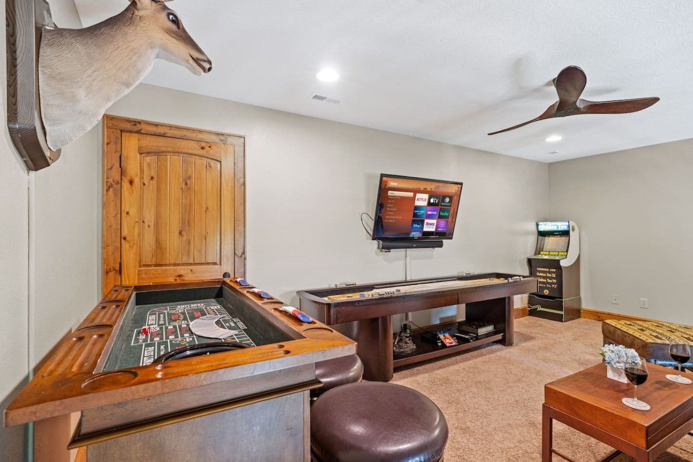 A room with a pool table, a mounted deer head, a television, and a gaming machine.