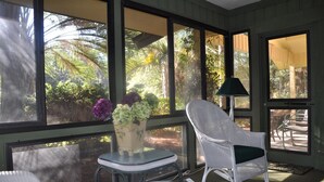 A sunlit room with large windows, a wicker chair, a small table, and a lamp. - SUPER VALUE VACATION HOUSE: PRIVATE BEACH, GOLF, POOL, BIKES
 (Hilton Head)