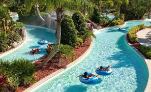 A water park with a winding pool, trees, and people on inflatable tubes.
