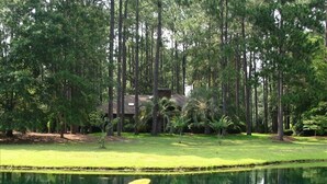A tranquil outdoor area with a pond, surrounded by tall trees and a building with a thatched roof. - SUPER VALUE VACATION HOUSE: PRIVATE BEACH, GOLF, POOL, BIKES
 (Hilton Head)