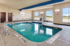 Une piscine intérieure sans panneaux indiquant l’interdiction de plonger, avec un poste de surveillance pour les sauveteurs et un escalier pour entrer dans la piscine.