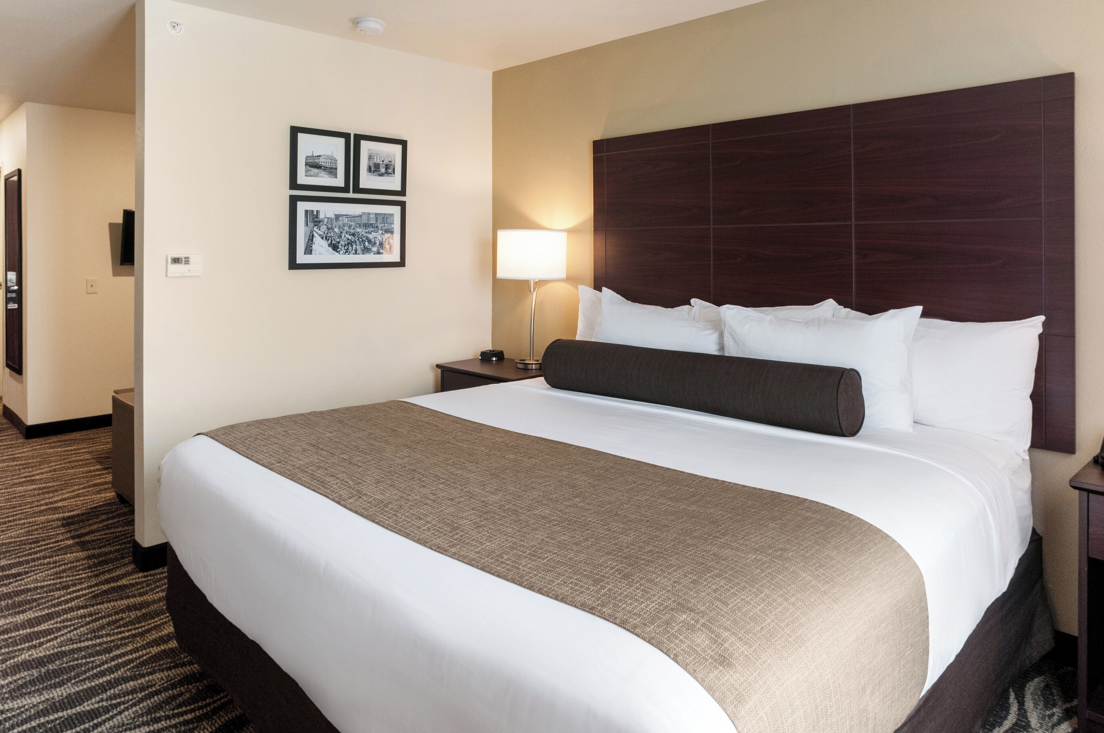 A hotel room with a large bed, a nightstand with a lamp, and three framed pictures on the wall.