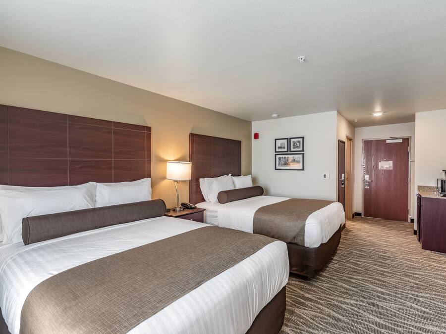 Une chambre d’hôtel avec deux lits, un bureau, une lampe et une porte donnant sur une salle de bain.