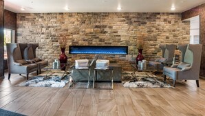 A modern living room with a stone wall, two sofas, a coffee table, and a flat-screen TV. - Cobblestone Hotel & Suites - Appleton International Airport (Neenah)