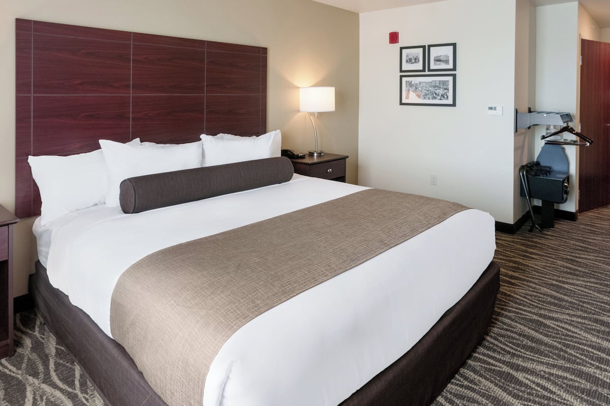 Une chambre d’hôtel avec un grand lit, une table de chevet avec une lampe, un bureau avec une chaise et un porte-manteau.