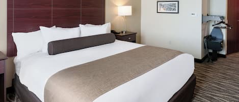 A hotel room with a large bed, a nightstand with a lamp, a desk with a chair, and a coat rack.