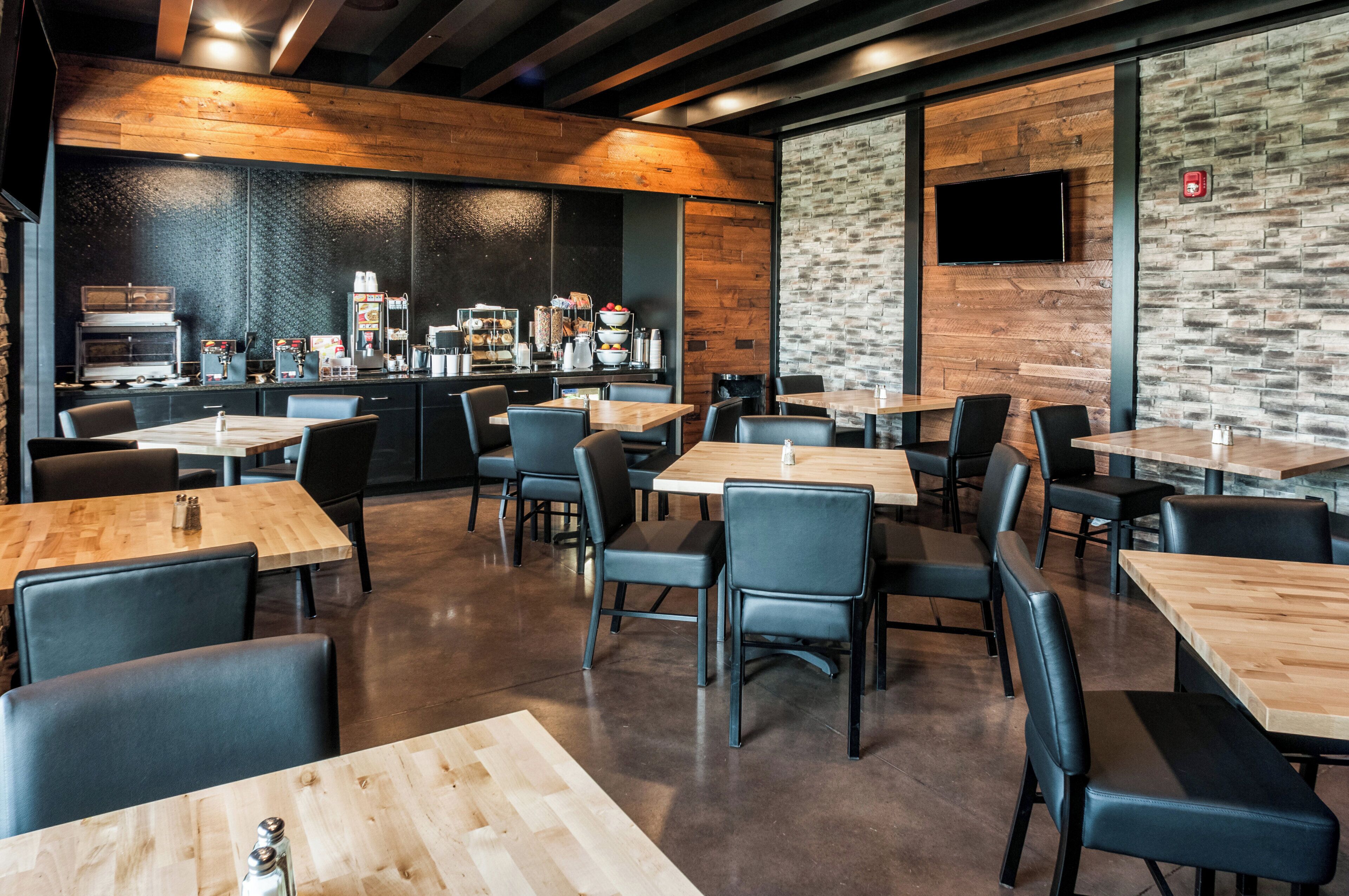 Een modern restaurant met houten tafels en zwarte stoelen, een koffiebar en een stenen muur.