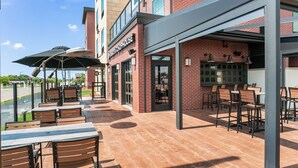 An outdoor patio area with tables and chairs, a brick building with a sign reading "WISCONSIN CHOPHOUSE," and a covered seating area. - Cobblestone Hotel & Suites - Appleton International Airport (Neenah)