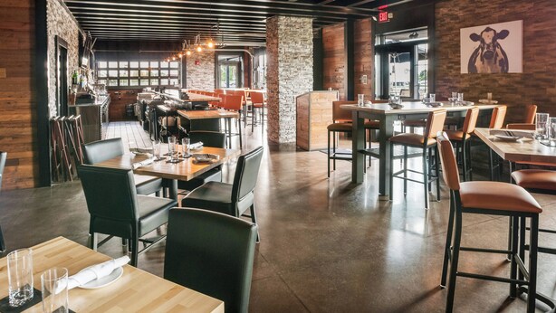 A modern restaurant with wooden and stone accents, multiple dining areas, and a view of the street. - Cobblestone Hotel & Suites - Appleton International Airport (Neenah)