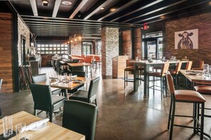 Un restaurante moderno con detalles de madera y piedra, varias zonas de comedor y vistas a la calle.