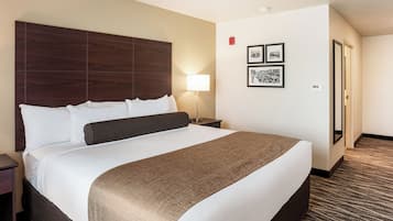 Habitación de hotel con una cama grande, una mesita de noche, una lámpara y dos cuadros en la pared.