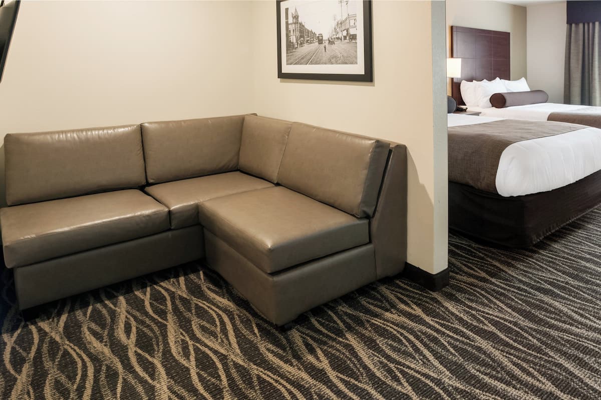 Une chambre d’hôtel avec un grand canapé en forme de L, un lit avec du linge de lit blanc et un tableau encadré au mur.
